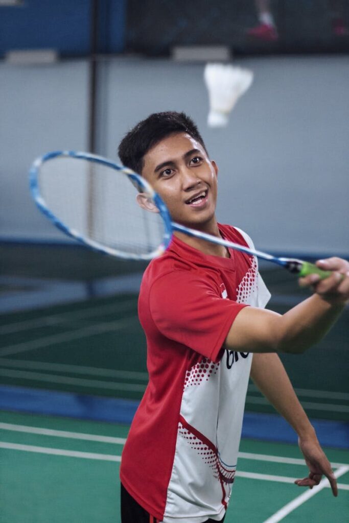 Focused young athlete playing badminton in an indoor court with racket and shuttlecock.