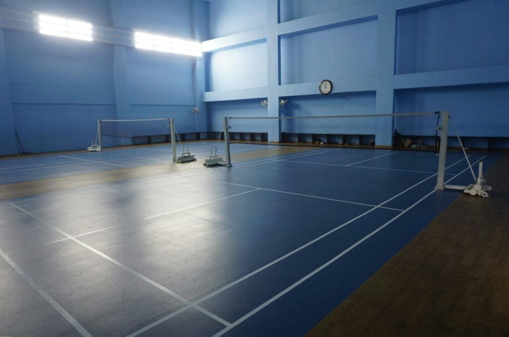 Indoor badminton court with blue walls and floor.