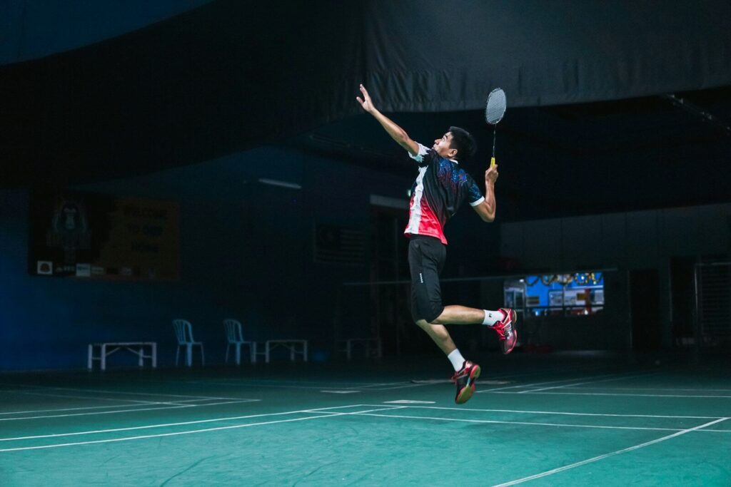 man in white and red crew neck t-shirt and black shorts playing badminton